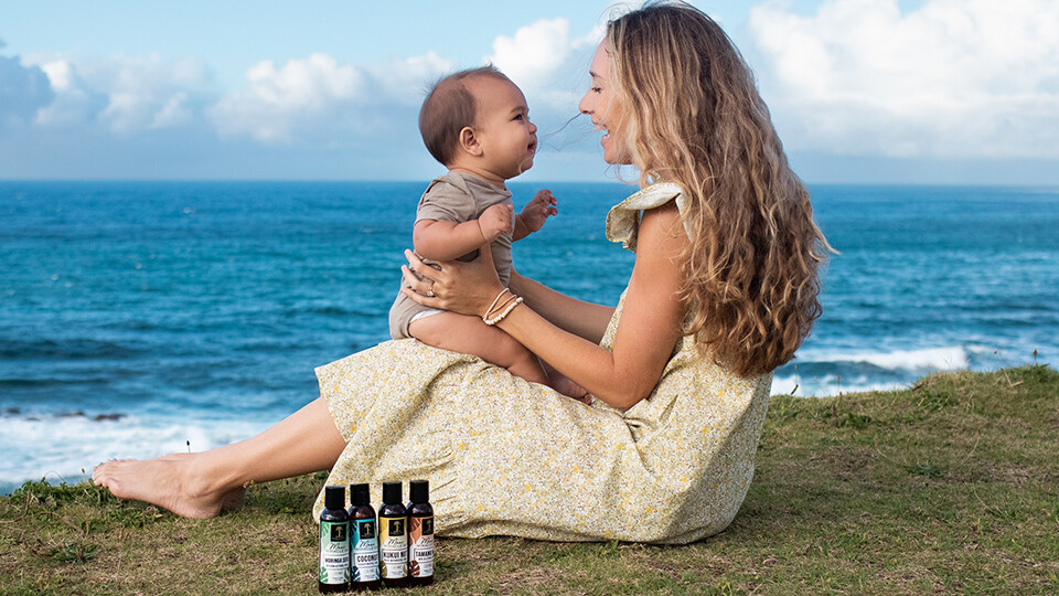 Mother Holding Baby on Beach with 4 Island Essence Oil Bottles
