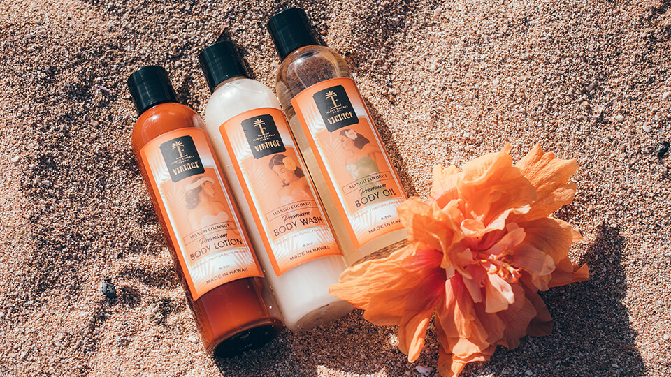 3 Mango Island Essence Products on Beach with Loofah