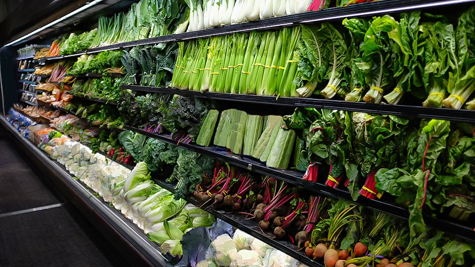A wide produce aisle stocked with fresh leafy greens and vegetables at a local Hawaii grocery store.