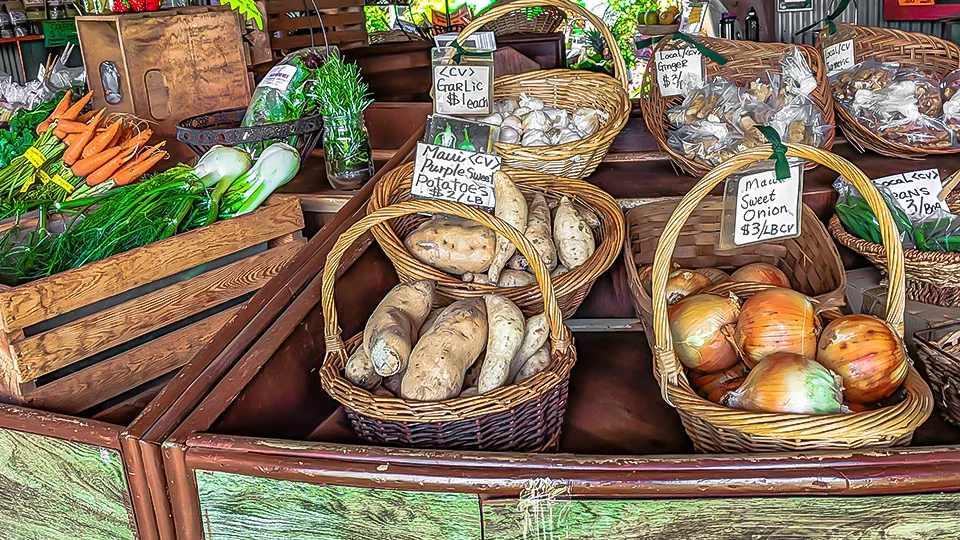 Baskets filled with sweet potatoes, onions, garlic, carrots, and leafy greens at a Hawaiʻi organic farm market.