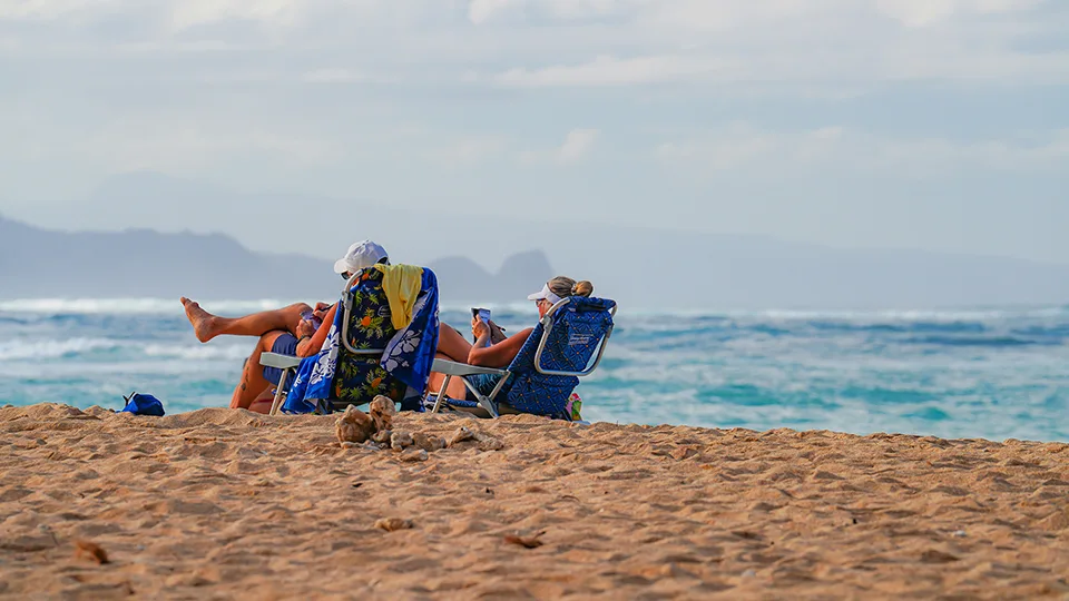 Beachgoers sitting in chairs near the water's edge at Ho‘okipa Beach on a breezy afternoon.