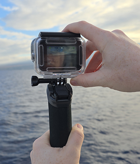 GoPro camera held over the ocean during a Maui snorkeling tour with Maui coastline in the background -