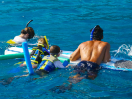 Mother, father, and their two sons floating on a surfboard Maui snorkel trip